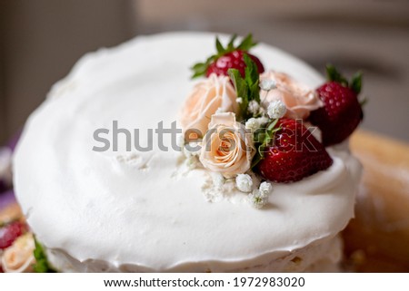 birthday cake with a decor of natural flowers and strawberries on a wooden board with roses and pionies on the vackground. vanilla biscuit, cream cheese. cake for a holiday