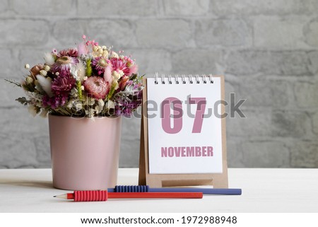 november 07. 07-th day of the month, calendar date.A delicate bouquet of flowers in a pink vase, two pencils and a calendar with a date for the day on a wooden surface..
