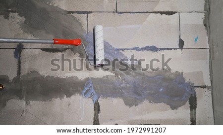 Painter paints wall with paint roller white. Painter man at work with a paint roller. The worker primes the wall with a roller.