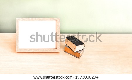 Two old books next to an empty wooden photo frame on a wooden table on a green background. A composition with a blur effect.