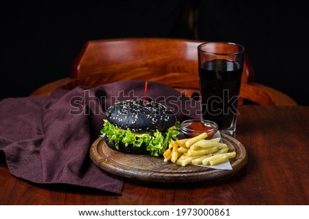 Black burger with french fries and ketchup on wooden table.