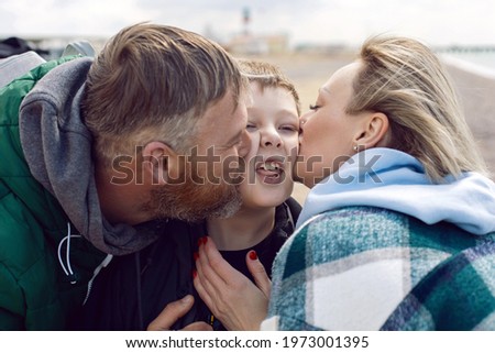 family mom and father kiss teen son on the cheek outside