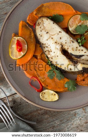 plate with baked halibut steak with lime and sweet potato on the table