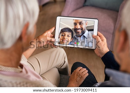 Senior couple doing a video call with son and grandson during covid19 pandemic. Happy indian father with child greeting in video conference his parents. Hands of old grandparents using digital tablet. Royalty-Free Stock Photo #1973009411