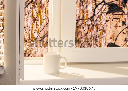 open window with a cup of coffee on the windowsill in a summer sunset evening 