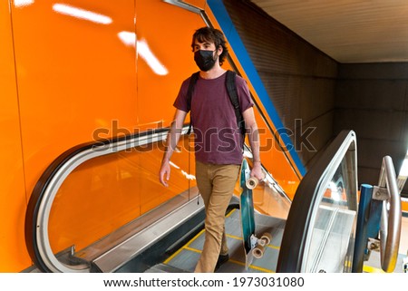 Horizontal view of young man with skateboard going up in the underground escalator in Madrid. Social distance and covid concept in Spain.