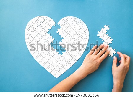 White puzzle in heart shape. White details of puzzle in hands on blue background.