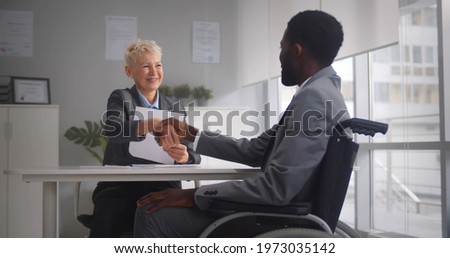 African disabled job candidate and mature female employer shaking hands and smiling at camera. Afro-american male applicant in wheelchair handshaking with hr manager