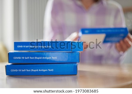 Close Up Of Woman At Home Reading Instructions On Supply Of Covid-19 Rapid Antigen Self-Testing Kits 