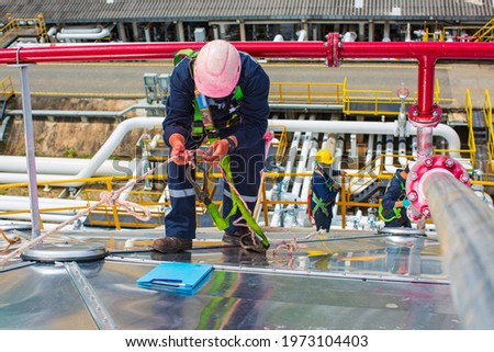 Male workers rope access height safety connecting with a knot safety harness, clipping into roof fall arrest and fall restraint anchor point systems ready to ascending, construction site oil tank dome Royalty-Free Stock Photo #1973104403