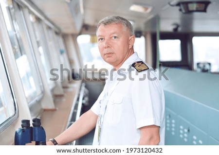 The captain of a cargo ship in a white shirt keeps order from the captain's bridge.
