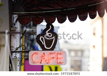 Glowing neon sign of a cafe with cup of coffee under a canopy.