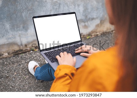 Mockup image of a woman holding and using laptop computer with blank white desktop screen in the outdoors