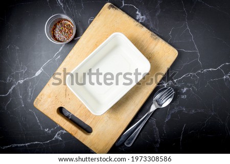 Empty rice box was placed on a cutting board with cutlery and dipping sauce on a black marble background. Rice boxes made from recycled bagasse, it can biodegradable. Meal box for delivery. top view.