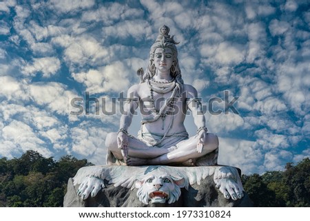 Statue of meditating Hindu god Shiva against the sky and clouds on the Ganges River at Rishikesh village in India, close up