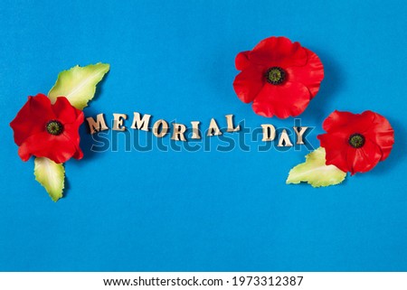 Text Memorial Day and a poppy flowers on blue background. Flat lay design for banner or greeting card.