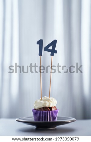Birthday or anniversary cake concept. Homemade chocolate birthday cupcake with creamy topping and number 14 fourteen on black plate and bright background. High quality vertical image