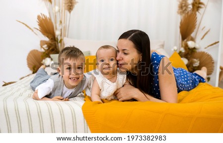 A brunette mother with a small son and daughter lies on the bed in the room. Happy family. Mother's Day