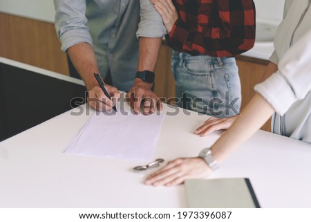 Close up of successful female realtor tightens a deal. Young real estate agent successfully closed deal a for sale of country house to family couple man signing agreement, standing at modern kitchen 
