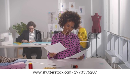 Young african woman designer entering office and greeting colleagues at workplace. Multicultural professional stylists working in workshop designing new clothes