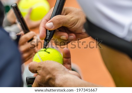 Tennis player signs autograph on a tennis ball after win, closeup photo showing tennis ball and hands of a man making signature. Royalty-Free Stock Photo #197341667