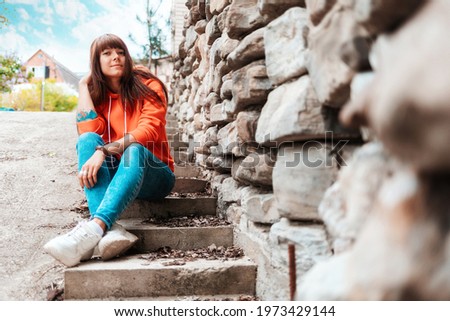 A young smiling woman with tattoed hand sits on the stone old stairs. Outdoor.