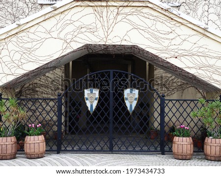 Black lattice gates decorated with shields with symbols surround the building overgrown with vines