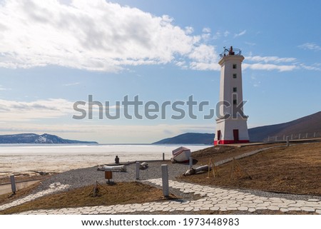 Lighthouse (leading beacon) on the coast of the sea bay. View from the shore to the ice-covered bay. Nagaev Bay, Sea of Okhotsk. Park Lighthouse in the city of Magadan. Far East of Russia. Mid-May. Royalty-Free Stock Photo #1973448983