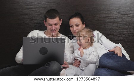 Happy family resting together in the evening at home with tablet. Online learning. Little child, daughter watching cartoon online using digital tablet, having fun with parental control, sitting on bed