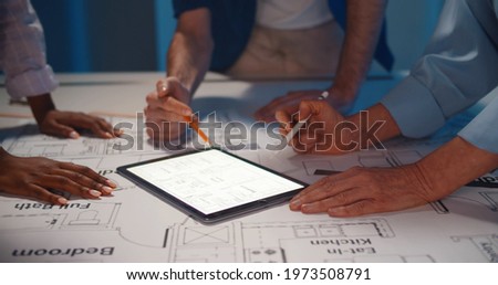 Close-up of team architects working on construction project in office. Cropped shot of engineers studying building blueprint and using digital tablet working together in office
