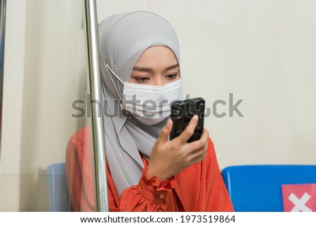 Asian muslim woman wear hijab head scarf and medical face mask and using mobile phone in the metro or train subway, public transport during coronavirus, or COVID 19 outbreak. Royalty-Free Stock Photo #1973519864
