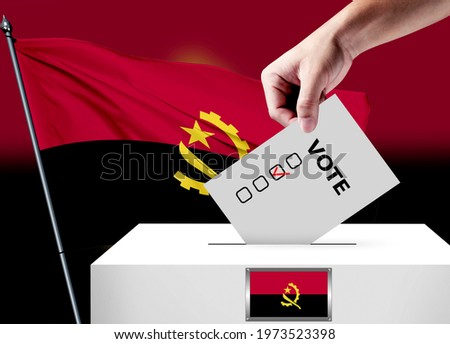 Elections in the Angola. The hand that puts the game in the ballot box. Angola flags in the background. Country flag election.