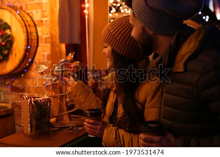 Lovely couple with cups of hot drinks spending time together at Christmas fair