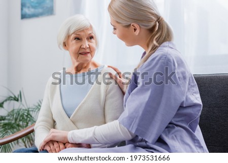 social worker touching hands of senior woman while talking at home Royalty-Free Stock Photo #1973531666