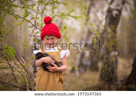 Little girl in a red hat in a spring forest plays with a rabbit in nature