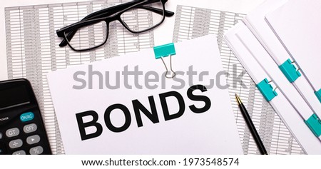 On the desktop are reports, documents, glasses, a calculator, a pen and paper with the text BONDS. Business concept