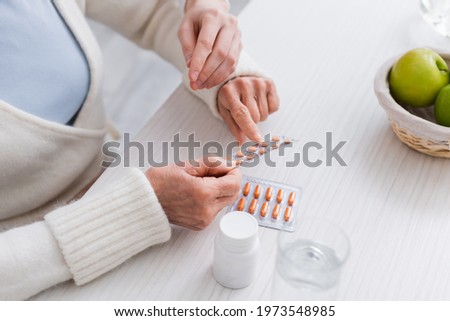 partial view of elderly woman pointing at pills near nurse and glass of water