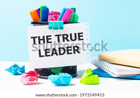 On a blue background - a stand with bright markers, notepads and multi-colored crumpled pieces of paper. A sheet of paper with the text THE TRUE LEADER.