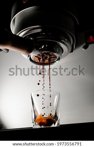 shot of hot espresso coffee is pulled through portafilter with wooden handle into clear glass. Process of making coffee Royalty-Free Stock Photo #1973556791