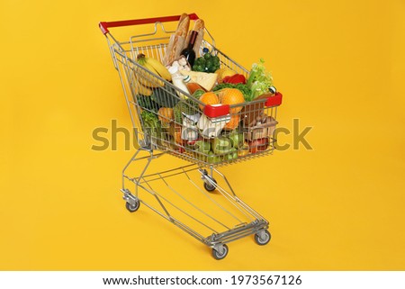 Shopping cart full of groceries on yellow background