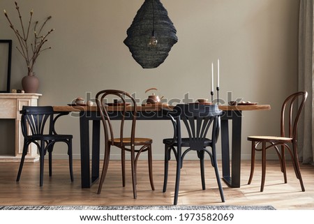 Stylish rustic interior of dining room with walnut wooden table, retro chairs, decoration, fireplace, dried flower, candlestick mock up picture frame and carpet in minimalist home decor. Template.