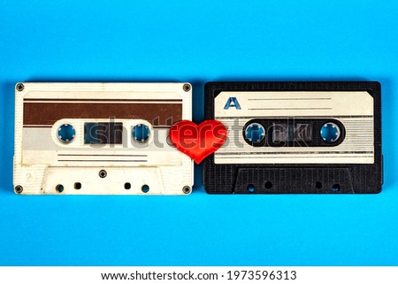 Two Old Audio Cassettes with a Red Heart on the Blue Paper Background closeup
