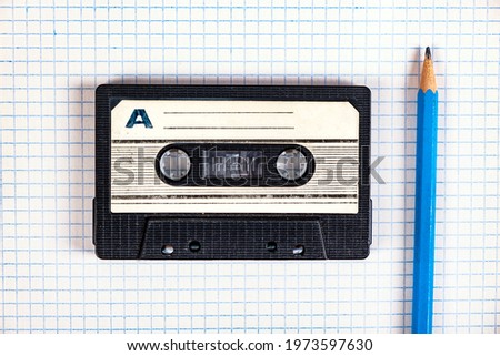 Old Audio Cassette with a Pencil on the Square Paper Background closeup