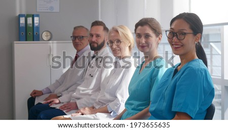 Medical team sitting in row and looking at camera. Doctors and nurses sitting on chair and smiling at camera attending medical seminar or lecture in hospital board room