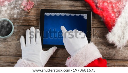 Composition of santa claus using tablet with blue christmas decoration on screen. technology and christmas tradition concept digitally generated image.