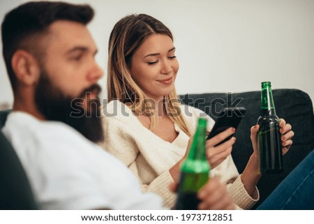 Young attractive couple drinking beer and watching television at home together on the weekend