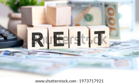 The word reit on wood cubes, banknotes and calculator on the background. Can be used for business, marketing and commerce concept
