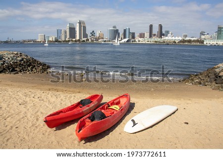 Two kayaks and a paddle board by a launching ramp in Coronado with view of of Downtown San Diego skyline across the bay. California, USA.