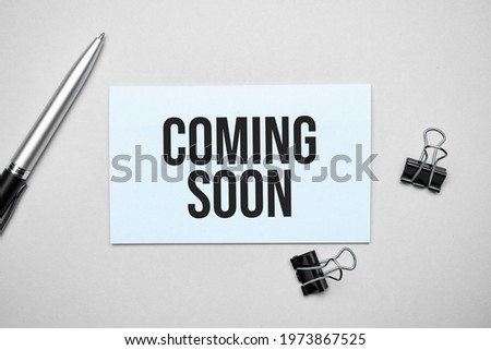 Top view of a business card with text Coming Soon , pen, paper clips on a colored background. Business concept.