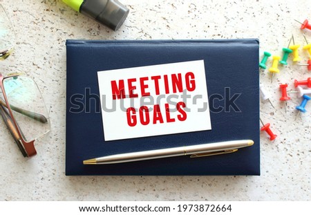 Text MEETING GOALS on a business card lying on a blue notebook next to the glasses and stationery. Business concept.